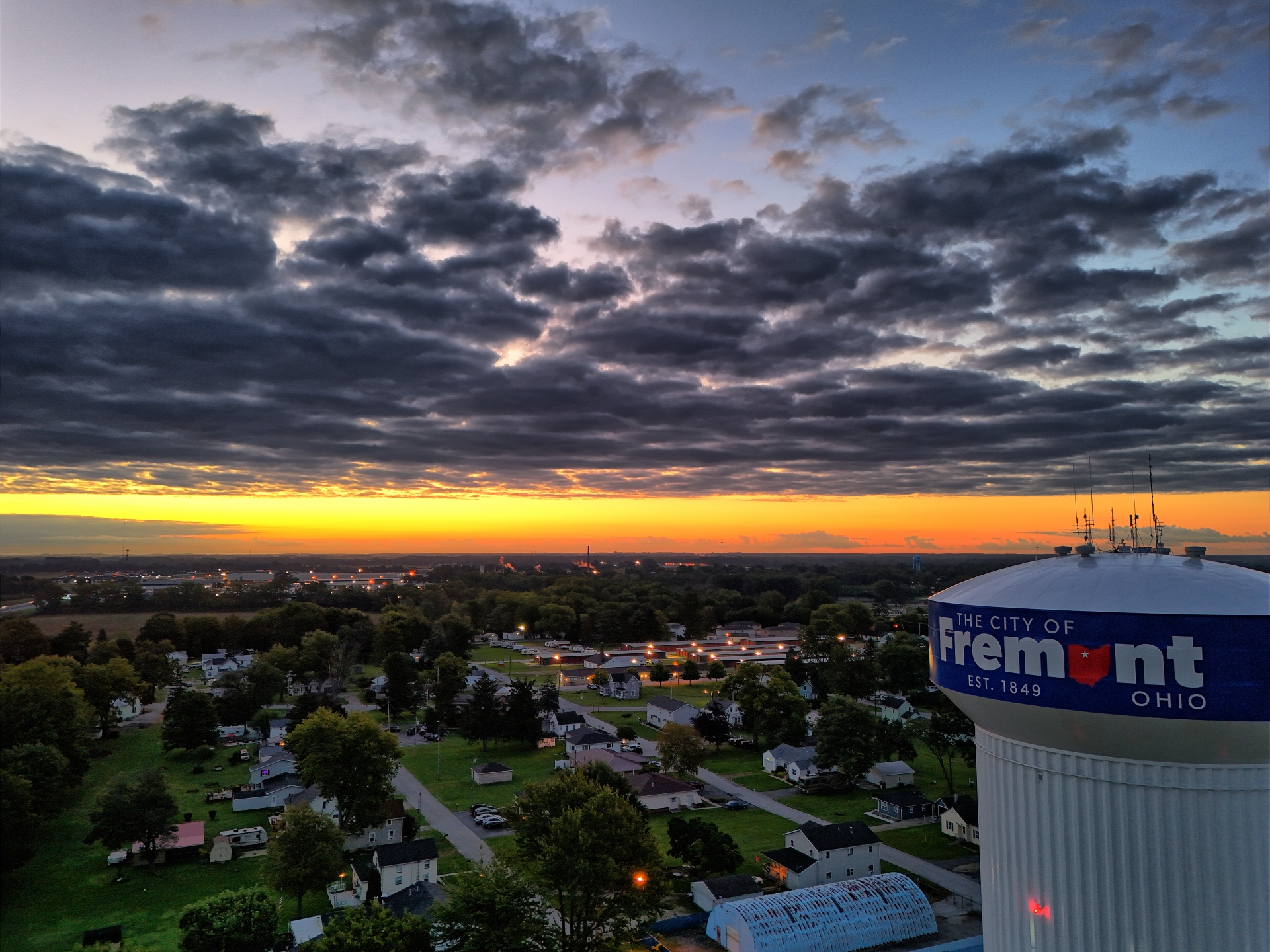 A drone capturing footage of a water tower in the middle of a town.