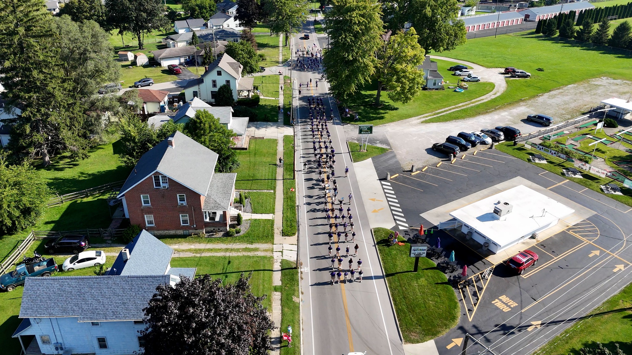 A bustling town viewed from above, with busy streets filled with cars and people moving in a parade.